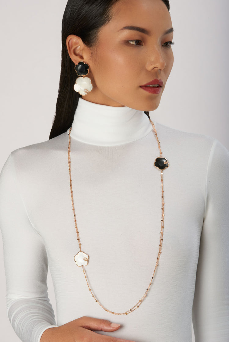 Pendant earrings and long necklace in 18k rose gold with black and white gemstones with diamonds on model in white turtleneck