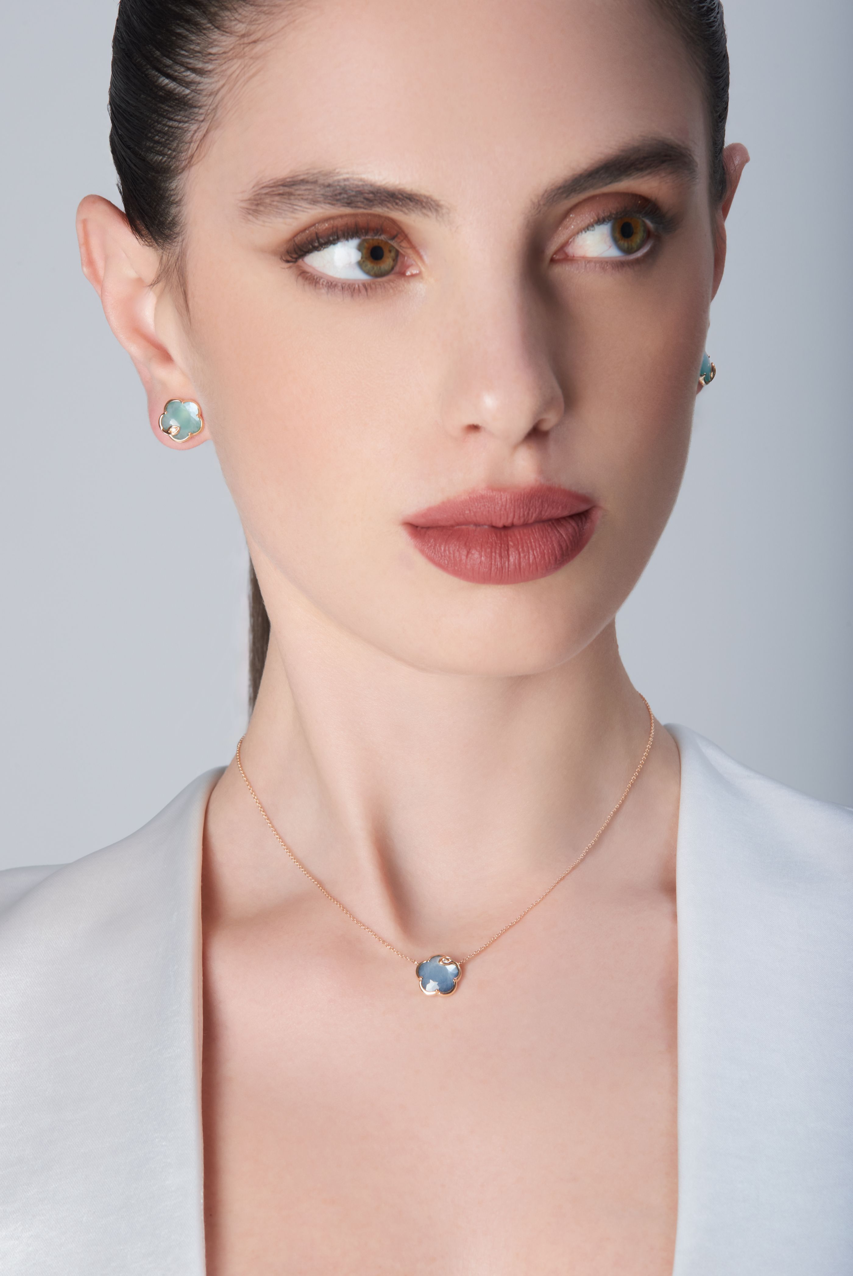 Earrings in 18k rose gold with green gemstone and diamonds and necklace in 18k rose gold with blue gemstones and diamonds on model in white blouse