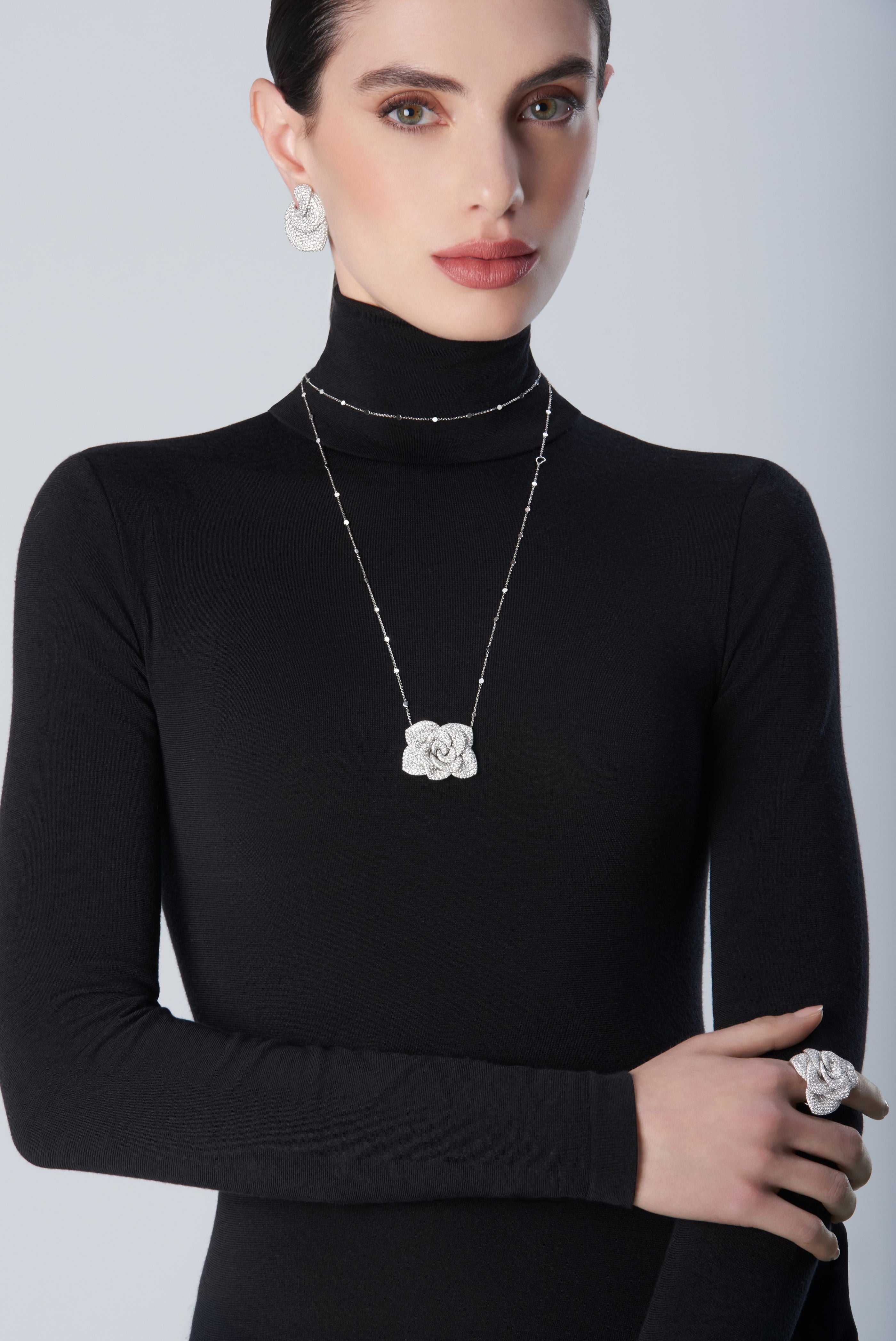 Woman wearing a black turtleneck with 18k white gold set of earrings, necklace and ring