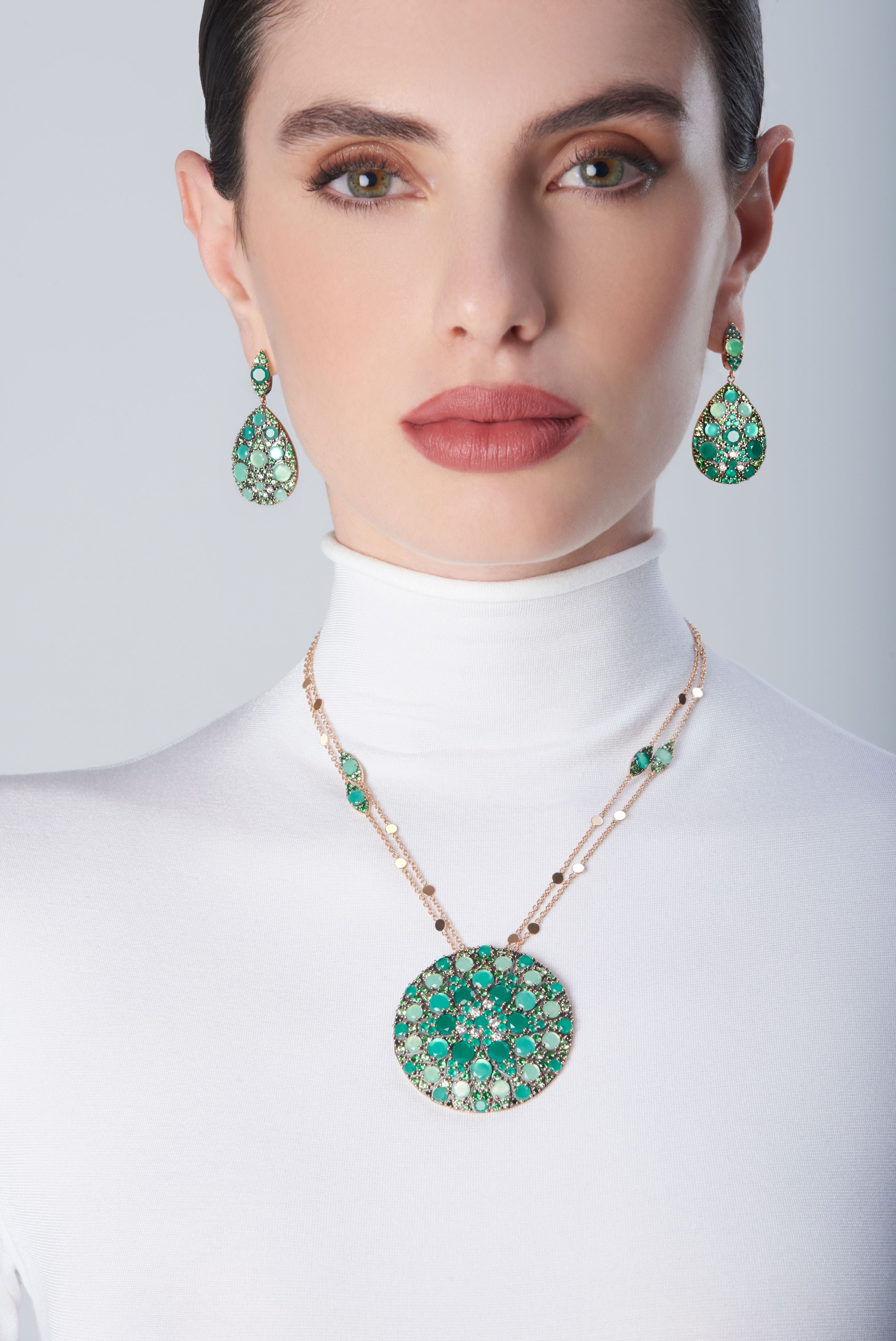 Earrings and necklace in in 18k Rose Gold with green precious gemstones on model with a white turtleneck