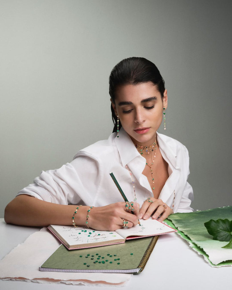 Model with earrings, rings and necklace in 18k Rose Gold and green gemstones wearing a white shirt.